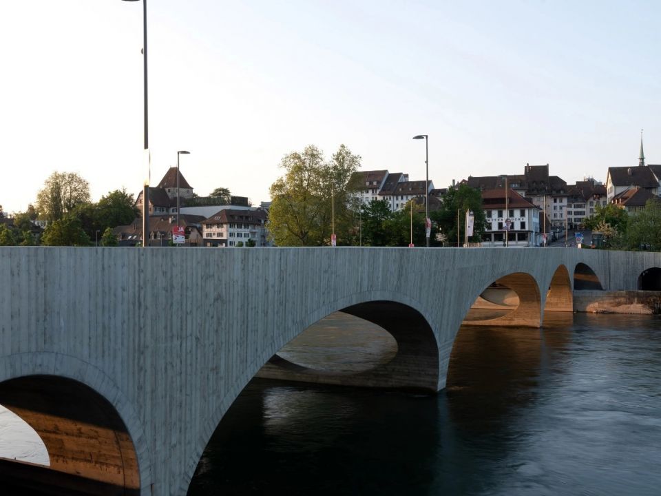 Скульптурный железобетонный мост в ШвейцарииВ швейцарском городе Арау построен скульптурный мост через реку Ааре по проекту архитектурной студии Christ & Gantenbein. Сооружение состоит из пяти арок различной ширины. Общая длина моста составляет 119 метров при ширине 17,5 м. На мосту выделены полосы для движения автомобилей, велосипедов и пешеходов. Он соединяет центр города с лесной зоной.Мост выполнен из монолитного железобетона и имеет сложную обтекаемую форму. Сооружение возведено на месте старого моста 1949 года постройки и частично использует его конструкции - подводные части двух опор.