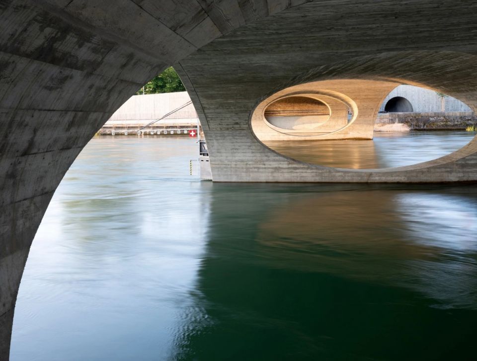 Скульптурный железобетонный мост в ШвейцарииВ швейцарском городе Арау построен скульптурный мост через реку Ааре по проекту архитектурной студии Christ & Gantenbein. Сооружение состоит из пяти арок различной ширины. Общая длина моста составляет 119 метров при ширине 17,5 м. На мосту выделены полосы для движения автомобилей, велосипедов и пешеходов. Он соединяет центр города с лесной зоной.Мост выполнен из монолитного железобетона и имеет сложную обтекаемую форму. Сооружение возведено на месте старого моста 1949 года постройки и частично использует его конструкции - подводные части двух опор.
