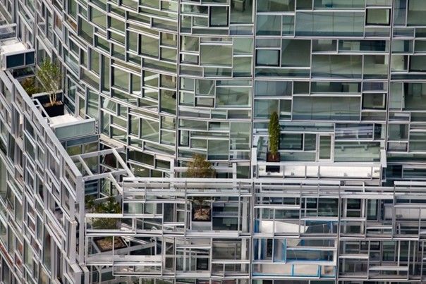 Необычный стеклянный фасад здания 100 11th Avenue в Нью Йорке11 авеню, 100 - жилое 23 этажное здание, возведенное в 2010 году по проекту Жана Нувеля в Манхэттене, Нью-Йорк. Здание обладает необычным, даже для Нью Йорка, фасадом.Фасад состоит из более чем 1650 стеклянных панелей, которые смонтированы под разными углами и обработаны специальными покрытиями. Это создает оптический эффект с переливанием оттенков на фасаде в зависимости от положения солнца и угла зрения.Стеклянные панели крепятся к алюминиевой решетке, анодированной серебром, которая, в свою очередь, передает нагрузки на стальной каркас фасада. С обратной стороны здание представляет собой почти монолитную черную кирпичную стену, изредка прорезанную небольшими оконными проемами. Благодаря архитектурному решению, окна на заднем фасаде, при взгляде изнутри здания, предстают подобием картин, развешанных на стене.