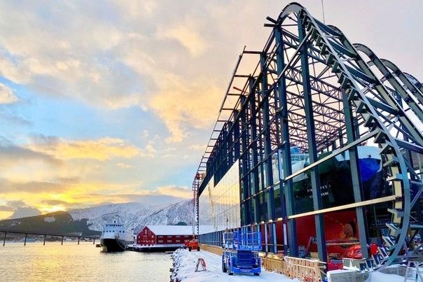 Hurtigruten Museum в НорвегииГлавной особенностью норвежского морского музея Hurtigruten Museum, посвященного истории одноименной судостроительной компании, является экспозиция восстановленного судна Finnmarken, которое имеет длину 140 метров. Корабль был спущен на воду в 1956 году и долгое время являлся символом компании.После вывода из эксплуатации судно некоторое время было выставлено на суше, под открытым небом, и фактически использовалось в качестве музейного экспоната. Однако вследствие отсутствия эксплуатационной поддержки, под воздействием атмосферных осадков, конструкция стала приходить в негодность.В 2019 году архитектурной студией LINK arkitektur был разработан проект укрытия для корабля - огромный сухой ангар с панорамным остеклением фасадов. Площадь защитного сооружения составила 3600 квадратных метров. Сооружение выполнено в стальном каркасе и отделано двойными стеклопакетами. Торцы закрыты алюминиевыми панелями.